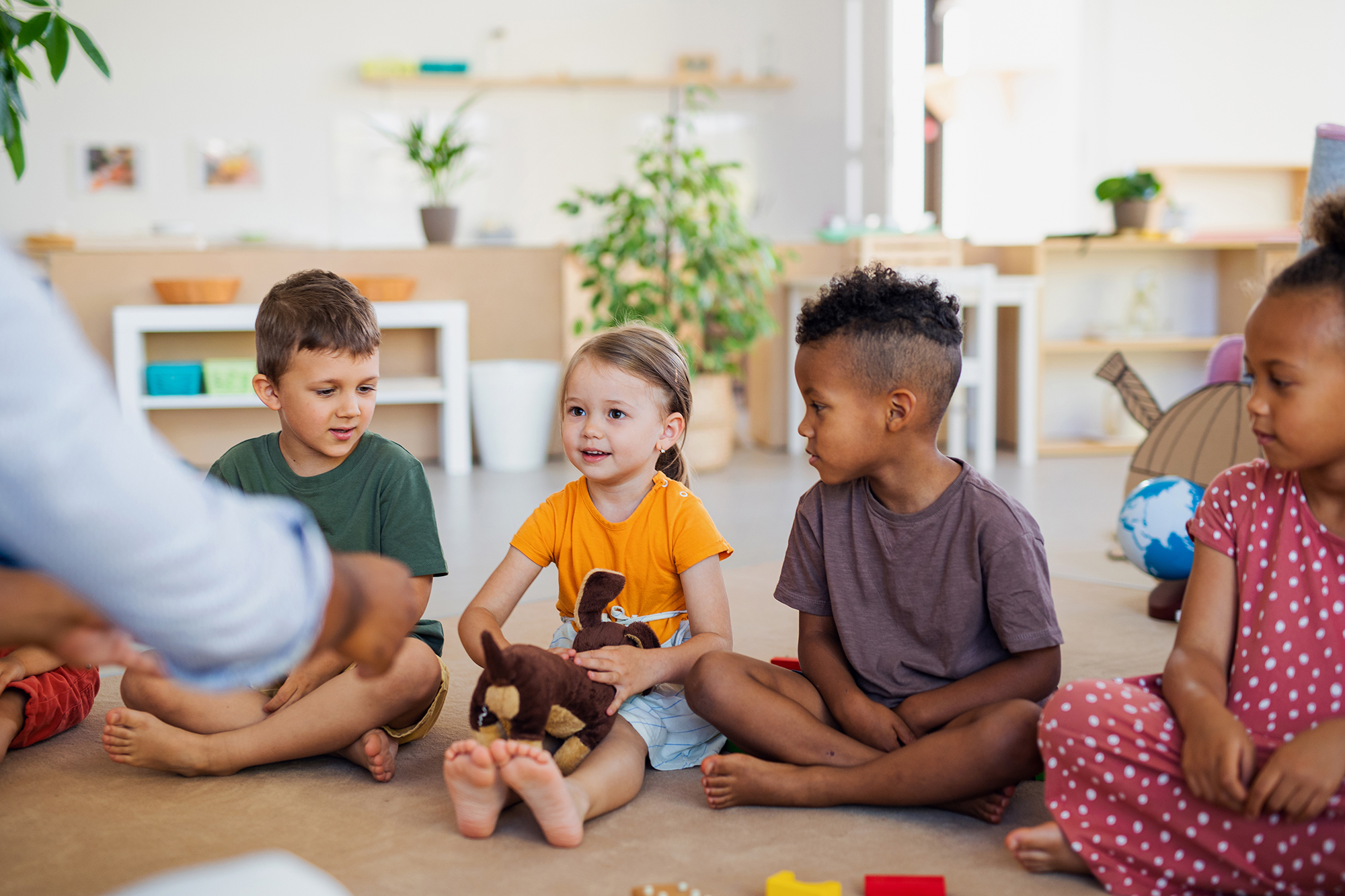 A group of small nursery school children sitting on floor indoors in classroom.